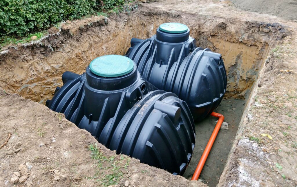 Zwei schwarze Erdtank Regenwasser Zisternen aus Kunststoff in ausgehobener Grube, bereit zur Installation im Garten