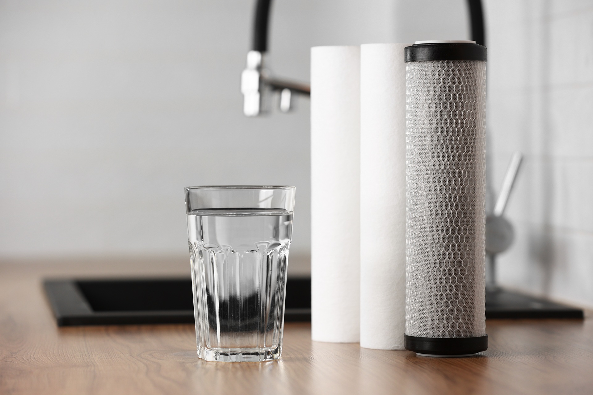 Glas frisches Trinkwasser neben moderner Filtertechnik | Wasserfilteranlage Küche