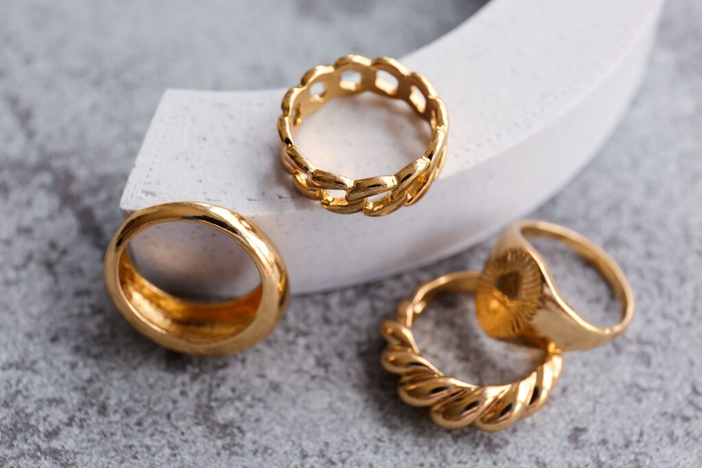 Dekoratives Podium mit verschiedenen goldenen Ringen auf grauem Grunge-Hintergrund