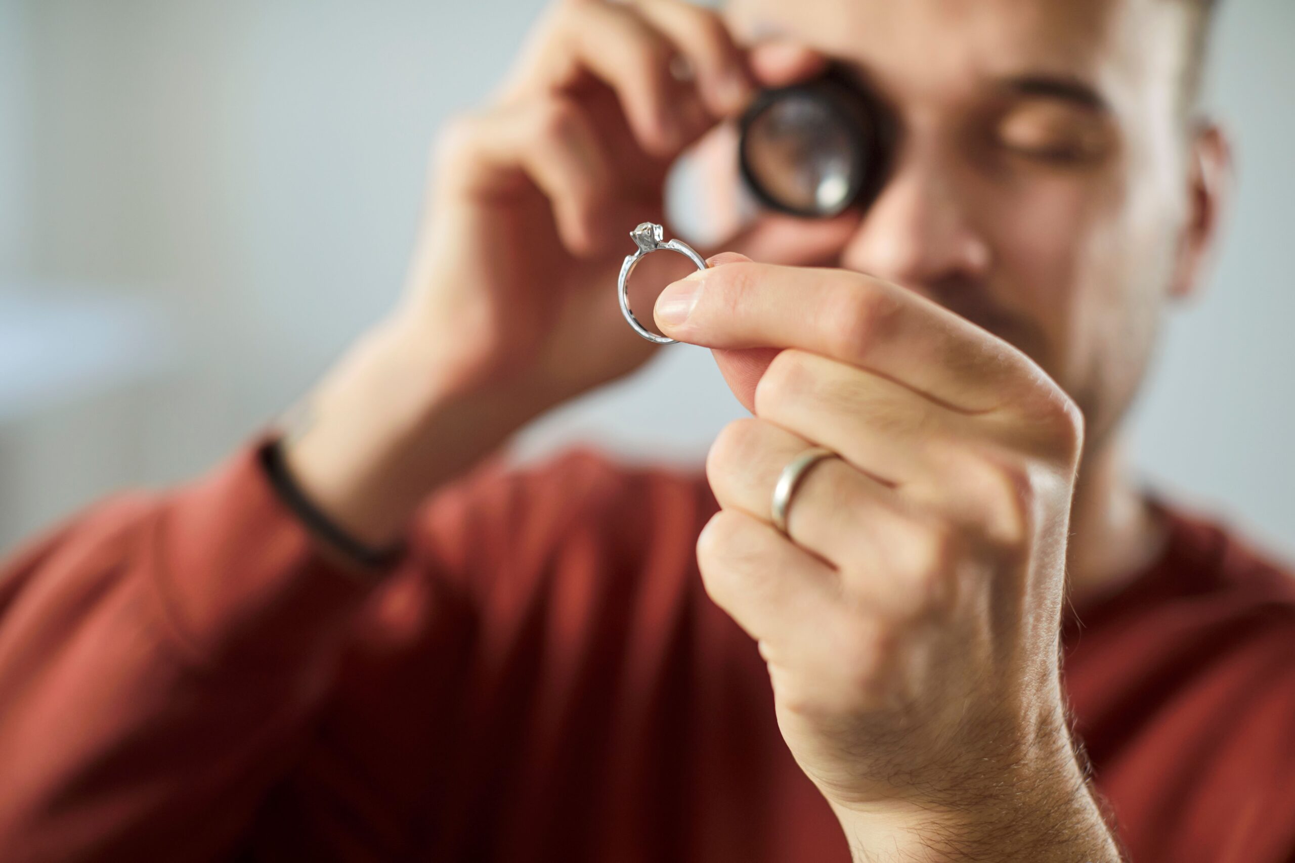 Nahaufnahme-Porträt eines jungen Mannes, Juweliers, der durch eine Lupe schaut und einen Goldring untersucht, um Schmuck mit Diamant zu bewerten.